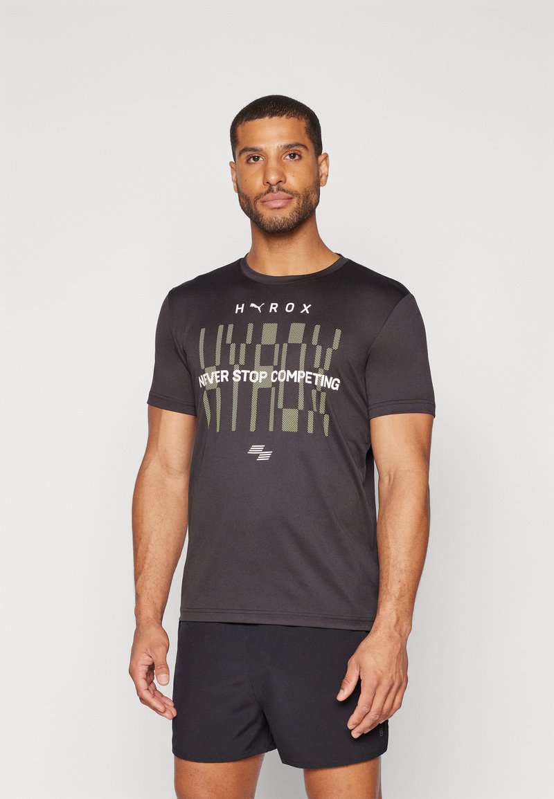 Camiseta deportiva negra de manga corta, con un texto gráfico verde que dice "HYROX NUNCA DEJES DE COMPETIR" y un logo en la parte frontal, hecha de una tela suave.