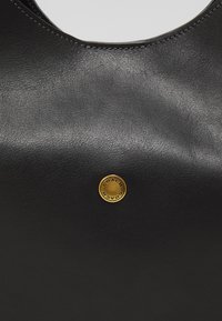 Bolso de mano de cuero negro con textura suave y un pequeño botón redondo de latón con el logotipo "Coach" en relieve.