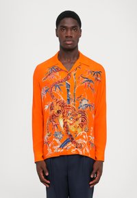 Kollane pika varrukaga särk, millel on detailne tiigri ja bamboo mustriline print, terava kaeluse ja esikülje nööpidega. Materjal tundub kerge.