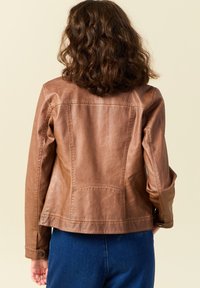 Giubbotto in pelle marrone con una vestibilità strutturata, cuciture visibili e tasche. Texture liscia con una finitura leggermente invecchiata.