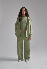 Completo coordinato di colore verde chiaro, composto da una felpa con zip, un crop top aderente e pantaloni larghi con vita elasticizzata. Tessuto morbido.