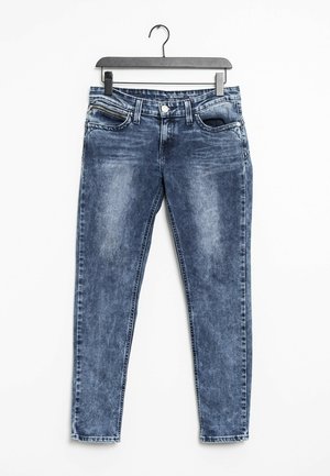 Vaqueros de mezclilla azul descoloridos con bolsillos delanteros y cierre de botón, colgados en una percha negra contra un fondo blanco.