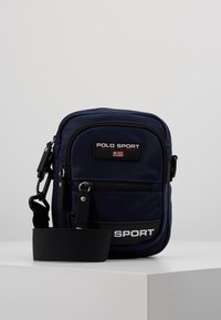 Borsa a tracolla blu navy con texture in nylon, dotata di una tasca frontale con zip, un'etichette personalizzata e una tracolla regolabile per maggiore comodità.
