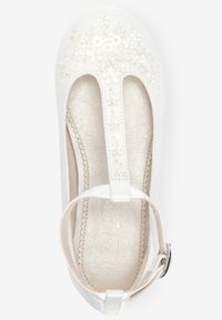 Chaussure de robe pour fille blanche avec bride T, fermeture à boucle et broderies florales sur la zone des orteils, dotée d'une semelle intérieure beige texturée.