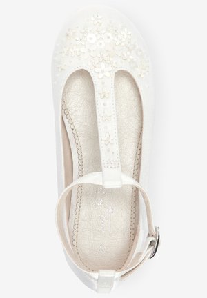 Witte meisjes schoen met T-strap, gespsluiting en bloemenborduursel op de neus, voorzien van een gestructureerde beige binnenzool.