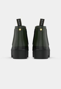 Botas de tornozelo em borracha verde com um acabamento texturizado, solas pretas e painéis laterais pretos. Apresenta um botão de destaque dourado e uma aba de puxar com o logótipo.