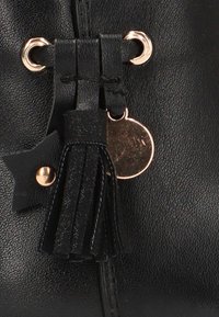 Bolso de cuero negro texturizado con borla, anillo metálico dorado, charm redondo y pequeño acento en forma de estrella, todo unido a través de ojales dorados.