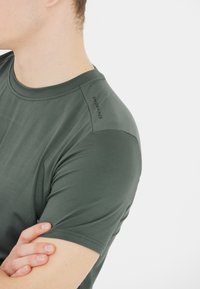 Mörkgrön atletisk t-shirt med rund hals, slät yta, figurnära design och en logotyp på axeln.