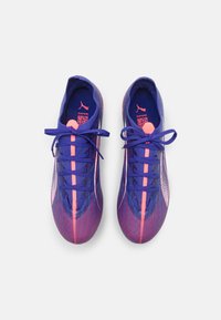 Zapatillas deportivas moradas con una parte superior de tela texturizada y detalles en rosa, cordones planos y un diseño contorneado para una apariencia elegante.
