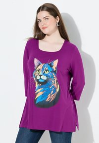 Violetti pitkähihainen tunika, jossa on eläväinen kissagrafiikka sinisen, oranssin ja keltaisen sävyissä. Pehmeää kangasta, jossa on nelikulmainen kaula-aukko ja sivurei'itykset.