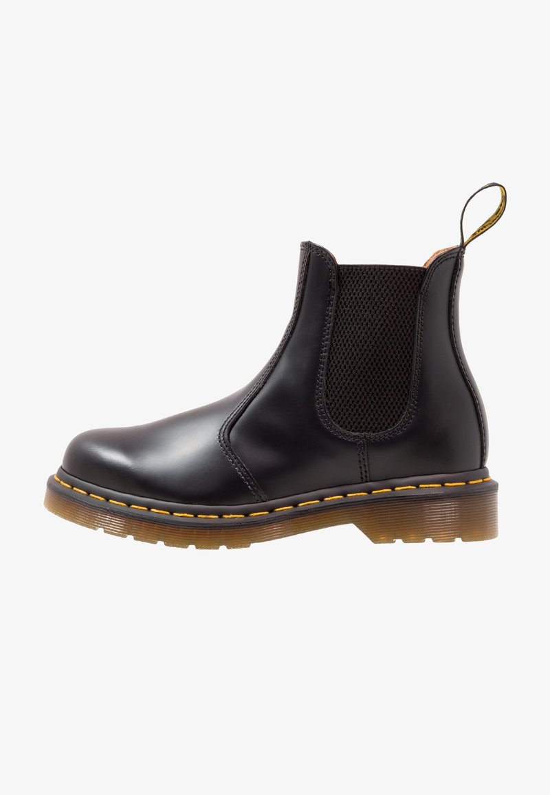 Botte Chelsea en cuir noir avec panneaux latéraux élastiques, couture jaune le long de la semelle, et une semelle extérieure en caoutchouc translucide marron.