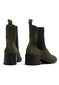 Oliwkowe zamszowe botki za kostkę z elastycznymi panelami bocznymi i masywnym czarnym obcasem. Posiadają pętelkę dla łatwego zakładania oraz gładką teksturę.