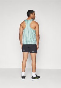 Mint green tank top with vertical stripes, open back design, paired with black shorts featuring reflective accent details. Black athletic shoes.