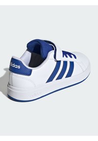 Baskets blanches avec des accents bleus et trois bandes, dotées d'un col rembourré et d'une sangle Velcro pour la fermeture. Semelle en caoutchouc texturée.