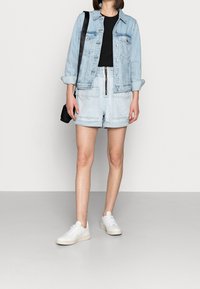 Světle modrá džínová bunda přes černé tričko, doplněná světle modrými šortkami s předním zipem a dvěma kapsami, a bílými teniskami.