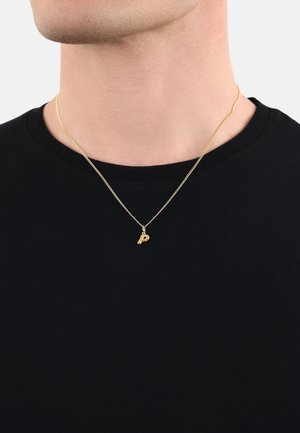 Goldene Halskette mit einem kleinen 'P'-Anhänger, die an dem Hals einer Person liegt. Der Anhänger hängt an einer dünnen, zarten Kette. Hintergrund in Schwarz mit einem T-Shirt.