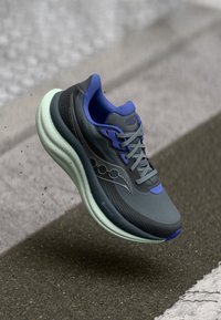 Gray athletic shoe with purple accents, textured mesh upper, laces, and a cushioned mint green sole, featuring subtle logo details.