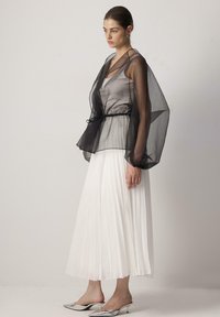 Prozirni crni gornji sloj s utegnutim strukom, preklopljen preko svijetlosivog gornjeg dijela i upareno s bijelom naboranom suknjom i srebrnim potpeticama