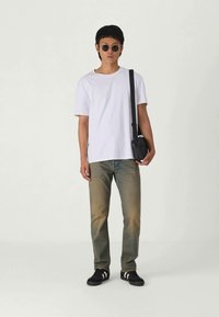 Hvit bomull t-skjorte, falmede blå jeans, svarte joggesko med hvite striper, runde solbriller og en liten svart skulderveske.