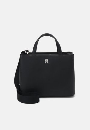 Sac à main en cuir noir avec double poignée, bandoulière amovible, et petit logo argenté "TH" centré sur le panneau avant.