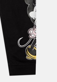 Pantalones jogging negros con un gráfico de un personaje con un lazo rosa y acentos amarillos en la parte baja de la pierna. Tejido suave con puños elásticos.