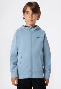Felpa con zip di colore blu chiaro, con un logo nero sul petto, tasche a marsupio e polsini a costine. Materiale morbido e vestibilità rilassata.