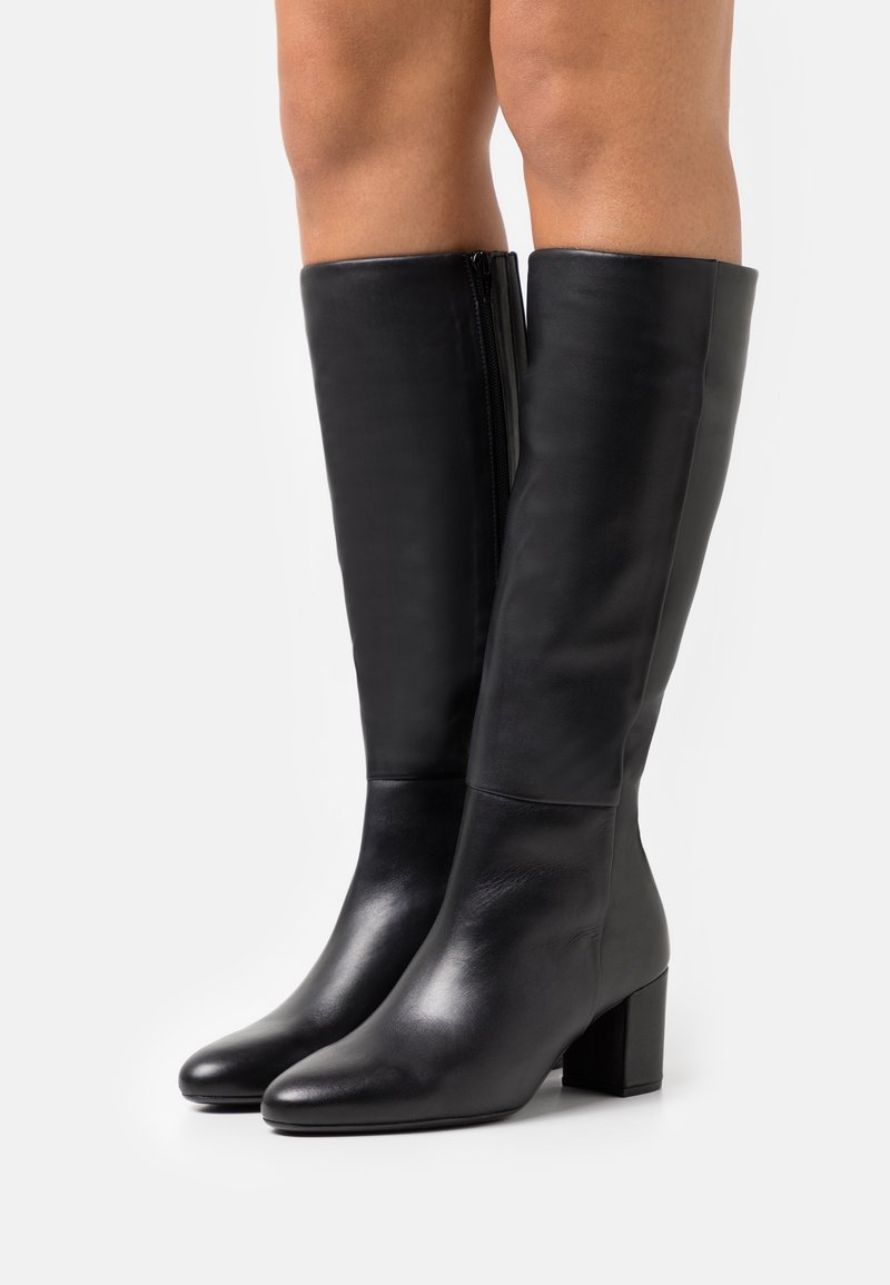 Bottes en cuir noir montantes jusqu'au genou, à texture lisse, talon bloc, bout arrondi, et détail zippé à l'arrière pour un enfilage facile.
