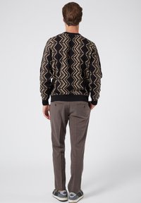 Maglione nero con un motivo a zigzag in beige e marrone chiaro, abbinato a pantaloni marroni e sneakers grigie. Texture lavorata a maglia e polsini a coste.