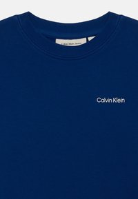 Sweatshirt azul de algodão com gola redonda ribeteada, apresentando um pequeno logótipo branco "Calvin Klein" bordado no peito.