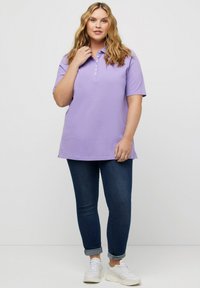 Jasnofioletowa koszulka polo z krótkimi rękawami, zapięciem na guziki i prostym dołem; zestawiona z ciemnoniebieskimi dżinsami i białymi trampkami.