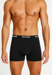 Muscular male torso wearing black boxer briefs with "SIXTH JUNE" logo on waistband, standing against plain light background.