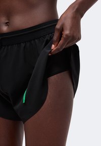 Gros plan d'une personne tirant la couche extérieure d'un short de sport noir pour montrer un short de compression noir intégré en dessous.