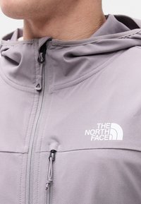 Κοντινό πλάνο ενός ατόμου που φοράει μωβ φούτερ με κουκούλα, με φερμουάρ στην μπροστινή τσέπη και το λογότυπο "The North Face" στο στήθος.