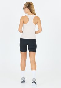 Hvid racerback tanktop og sorte cykeltights, der viser en glat tekstur. Tanktoppen har en tætsiddende pasform, der egner sig til sportstøj.