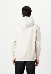 Witte hoodie met een relaxte pasvorm, ribbelmanchetten en -zoom. Gladde textuur en minimalistisch ontwerp zonder zichtbare logo's of patronen.