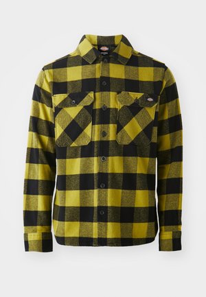 Flannel skjorte med et gult og sort ternet mønster, med knappelukning foran, to brystlommer og krave. Blød tekstur, lange ærmer.