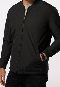 Giacca bomber nera con zip frontale, colletto e polsini a coste. Tessuto liscio, vita elasticizzata e tasche laterali. Design semplice e moderno.