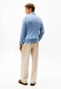 Jasnoniebieski sweter w prążki z dekoltem w serek i długimi rękawami, noszony na koszuli w kratę, połączony z beżowymi spodniami i brązowymi butami.