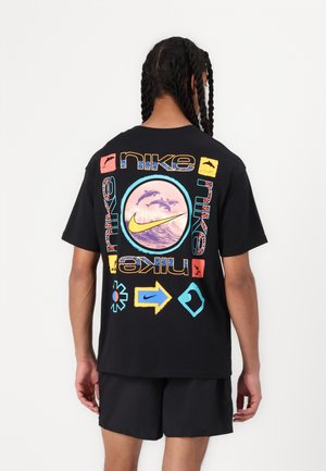 Osoba z zaplecionymi włosami w czarnej koszulce Nike z kolorowymi grafikami delfinów i fal oraz logo na plecach.