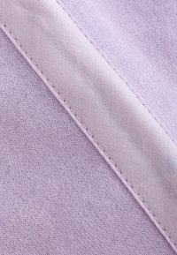 Detail světle fialové látky zobrazující diagonální šev s detaily šití na texturovaném pleteném pozadí.