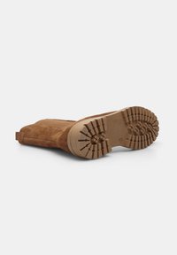 Bocanci din suede maro cu o talpă din cauciuc texturată. Bocancii au un tab pentru călcare ușoară și un design cu vârful rotund.