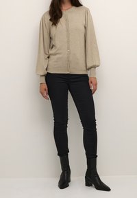 Béžový pletený kardigan s balónovými rukávy, zapínáním na knoflíky a žebrovanými manžetami, doplněný o černé skinny džíny a černé špičaté kotníkové boty.