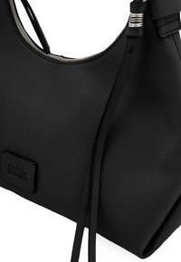 Borsa a tracolla in pelle nera con finitura testurizzata, forma curva, dettagli in metallo argentato e un logo del marchio in evidenza su una toppa rettangolare.