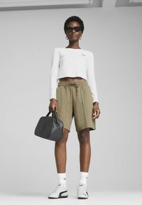 Top corto blanco de manga larga, shorts verde oliva, bolso negro con logo grabado, zapatillas gris y blanco, y gafas de sol.