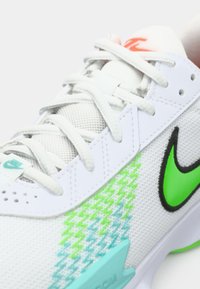 Hvide Nike sneakers med grønne og blå zigzag-mønstre, lys grøn swoosh og hvide snørebånd på mesh-overdelen.