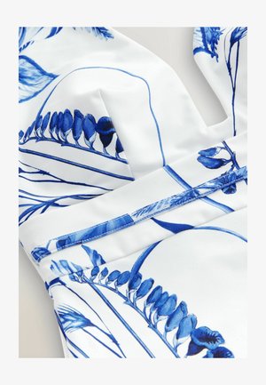 Weißer Stoff mit einem blauen Blumenmuster, das Blätter und Blüten zeigt; glatte Textur mit strukturierten Nähten und Akzenten.