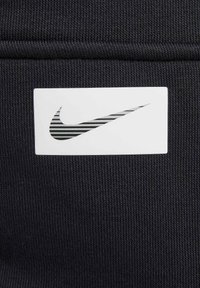 Svart tyg med vertikal textur har en vit rektangulär lapp med en svartvit randig Nike-logotyp.
