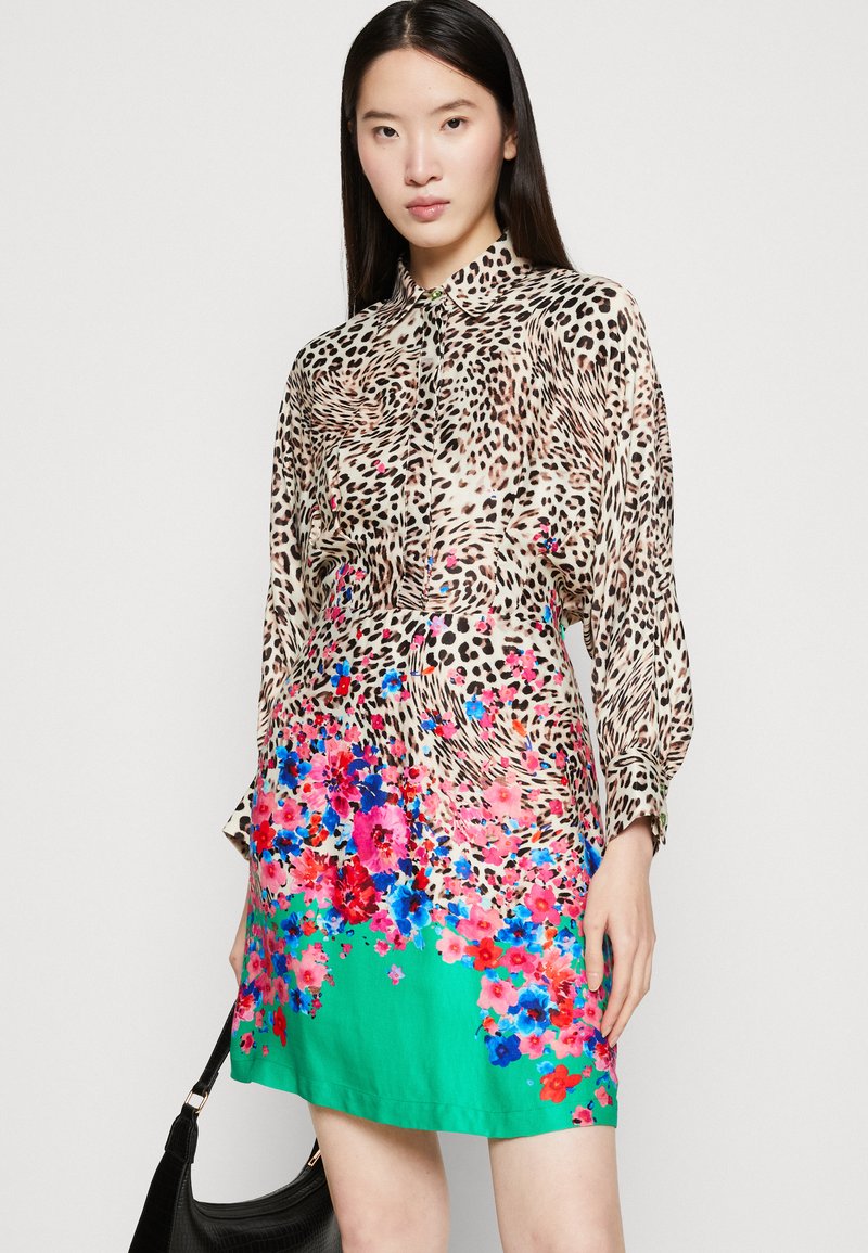 Robe chemise imprimé léopard avec des manches longues, accents floraux en rose et bleu, et une section inférieure verte ; le tissu semble léger et lisse.