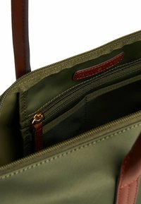 Olijfgroene tasinterieur met een ritsvak, leren trekband en zichtbare bruine leren schouderriem.