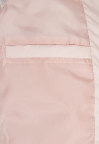 Világos rózsaszín textil sima felülettel, téglalap alakú zsebbel, varrással és látható zár nélkül.